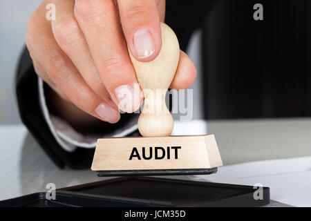 Primo piano della mano che tiene il timbro di gomma con segno di audit a tavola in office Foto Stock