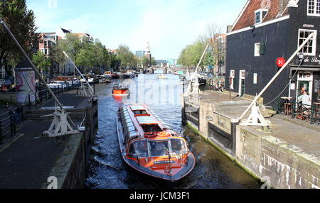 Canal Boat passando Sint Antoniesluis serratura tra Zwanenburgwal & Oudeschans canal, Amsterdam, Paesi Bassi, con il café De Sluyswacht (Goslerhuisje). Foto Stock
