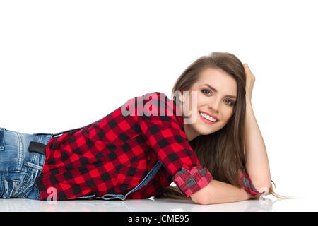 Sorridente giovane donna in rosso lumberjack shirt giacente su un piano e guardando la fotocamera. Vita studio shot isolato su bianco. Foto Stock