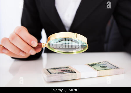 Sezione mediana del giovane imprenditrice scrutare le fatture del dollaro con lente di ingrandimento a scrivania da ufficio Foto Stock