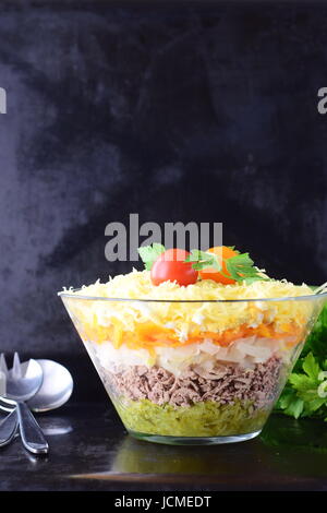 Insalata con fegato di pollo in strati con sottaceti,carota lessata, l'uovo, il formaggio in una ciotola di vetro su di un nero sfondo astratto. vista dall'alto. cibo sano conc Foto Stock