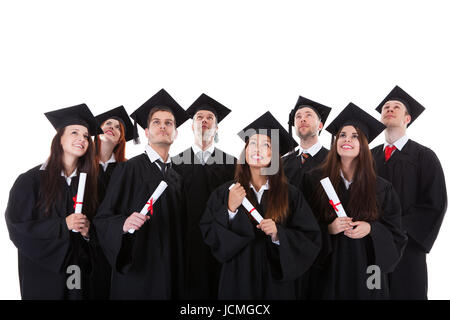 Sorridenti gruppo di diplomati multietnica vestita di nero academic abiti e cappelli mortarboard raggruppati in piedi vicino insieme con i loro certificati isolato su bianco Foto Stock