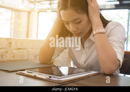 Giovane donna asiatica mettere mano sulla testa sensazione di stanchezza, frustrato e sottolineato dal duro lavoro mentre è seduto alla worklace in office Foto Stock