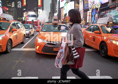 Donna crosswalk di attraversamento di fronte yellow cabs in serata in Times Square a New York City USA Foto Stock