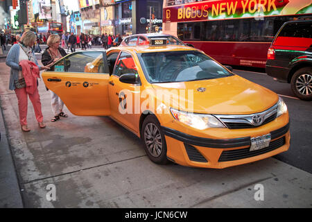Due donne a entrare in un taxi giallo in serata in Times Square a New York City USA Foto Stock