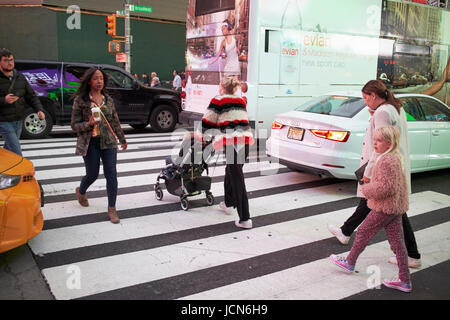 Donna spingendo bambino nel passeggino attraverso crosswalk nella trafficata e traffico di sera in Times Square a New York City USA Foto Stock