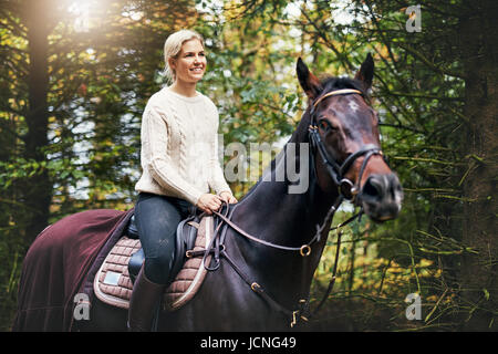 Ritratto di una donna sorridente a cavallo sullo sfondo di foglie verdi Foto Stock