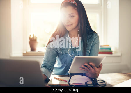 Allegro giovane imprenditore donna utilizzando laptop in auricolari e azienda tablet seduto in ufficio. Foto Stock