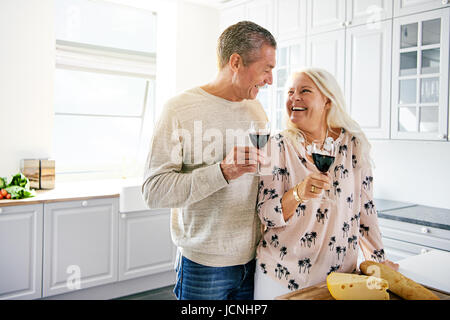 Ridendo affettuosa coppia in pensione di bere un bicchiere di vino insieme in cucina sorridente felicemente come essi si guardi negli occhi, con copia sp Foto Stock