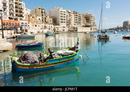 Un pescatore mende le sue reti nel suo Luzzu barca da pesca nel porto di St Julians Bay Malta su una soleggiata giornata estiva Foto Stock