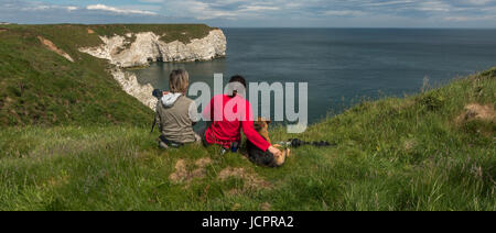 Due donne e un cane seduto sul clifftops per guardare fuori a guardare la fauna selvatica, bird spotting con telecamere, Flamborough, nello Yorkshire, Inghilterra, Regno Unito la fauna selvatica Foto Stock