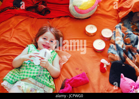 Bambino giacente sul letto disordinato con oggetti assortiti Foto Stock