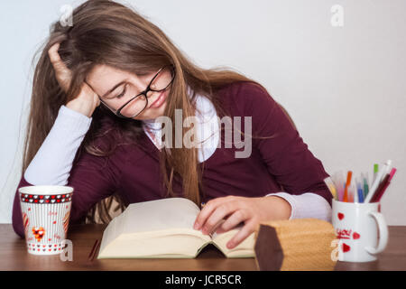 Bella carino bimba bionda con gli occhiali e vestito viola è stanco della lettura di un libro. Gli occhiali sono quasi caduto e di addormentarsi Foto Stock