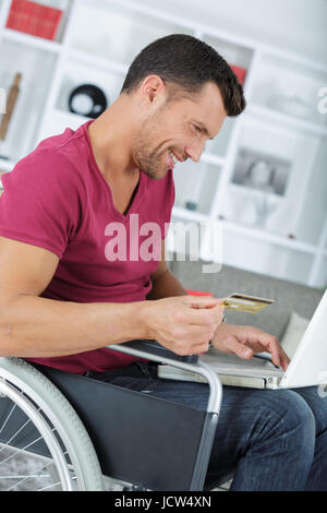 Uomo disabili in carrozzella utilizzando la carta di credito su internet Foto Stock