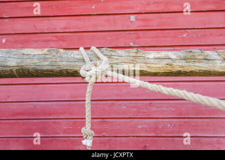 Corda allacciate in un nodo su un post di aggancio nella parte anteriore di un rustico rosso muro del granaio Foto Stock