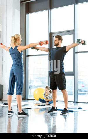 Persone Fitness esercizio con manubri mentre la ragazza seduta sul tappetino in studio fitness Foto Stock