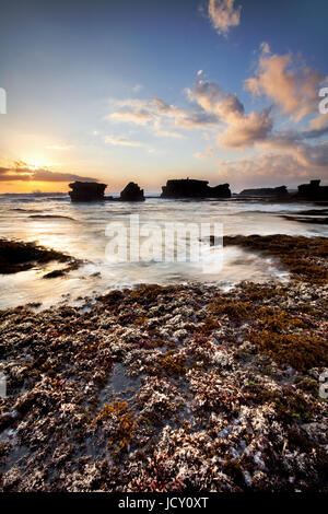 Alghe bianca sulla costa di Bali con il profilarsi di pile di mare. Una lunga esposizione seascape foto scattata con una lenta velocità di otturazione tecnica durante il tramonto Foto Stock