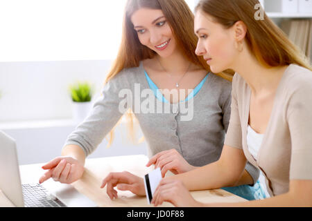 Due amici o sorelle di parlare tenendo una conversazione a tavola con laptop alla ricerca di ogni altro Foto Stock
