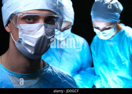 Tre chirurghi al lavoro operanti nel teatro chirurgico salvataggio di paziente e guardare la vita del monitor. Medicina di rianimazione team indossando maschere di protezione. Foto Stock