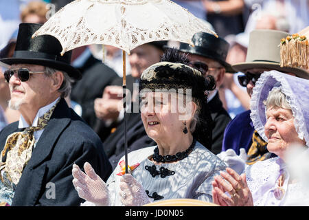 Tre persone sedute e battimani, tutti gli anziani, due donne e un uomo seduto sotto il sole in tutti vestiti fino a classe superiore costume vittoriano come parte del Broadstairs Dicken week festival. Centro Donna holding lacey sun ombrellone. Foto Stock