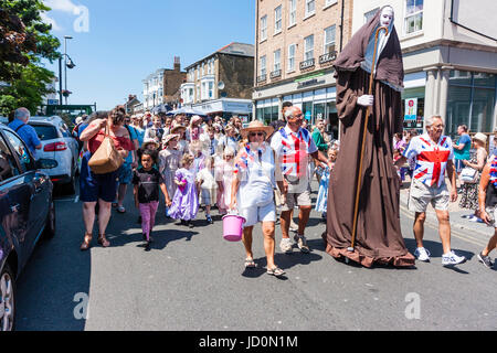 Inghilterra, Broadstairs. Dickens la settimana del Festival, la sfilata principale su Broadstairs High Street con vari gruppi in costume Vittoriano. Due uomini in Unione Jack t-shirts portante un 12 piedi di altezza effige di una monaca chiamato 'il gigante del Minster'. Foto Stock