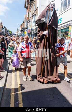 Inghilterra, Broadstairs. Dickens la settimana del Festival, la sfilata principale su Broadstairs High Street con vari gruppi in costume Vittoriano. Due uomini in Unione Jack t-shirts portante un 12 piedi di altezza effige di una monaca chiamato 'il gigante del Minster'. Foto Stock