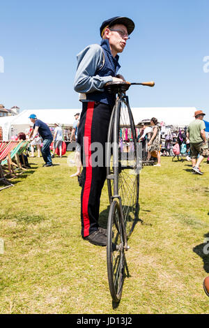 Uomo in piedi tenendo la sua Penny Farthing precoce bicicletta vittoriano sull'erba durante Broadstairs Dickens settimana. Usura uniforme e tappo. Angolo basso punto di vista. Foto Stock