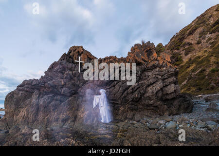 Roccia lavica con una croce bianca su di essa, con un uomo in bianco toccando un volto nella roccia Foto Stock