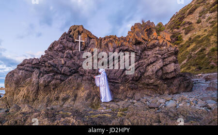 Roccia lavica con una croce bianca su di essa, con un uomo in bianco di toccare la roccia Foto Stock