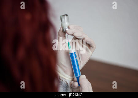 Giovane medico prepara una iniezione ad un paziente, il liquido iniettato nell'ago, tenendo molto attentamente Foto Stock