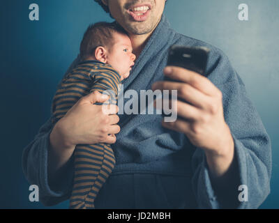 Un giovane padre in un accappatoio sta prendendo un selfie con suo Figlio bambino Foto Stock