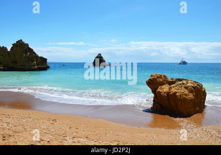 Lavaggio onde attorno ad una roccia a Praia Dona Ana e yacht in background, Algarve, PORTOGALLO Foto Stock