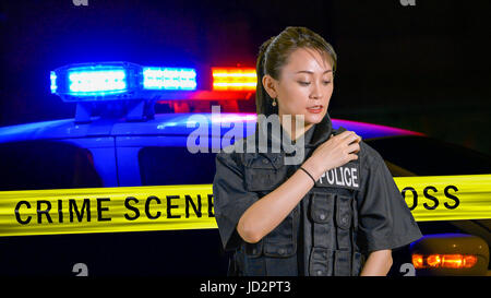 Americano asiatico poliziotta utilizzando radio della polizia con sirena e nastro di confine in background Foto Stock