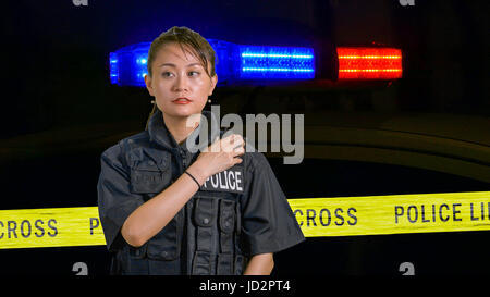 Americano asiatico poliziotta utilizzando radio della polizia con sirena e nastro di confine in background Foto Stock