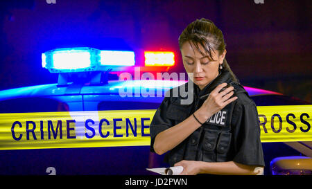Americano asiatico poliziotta utilizzando radio della polizia con sirena e nastro di confine in background Foto Stock
