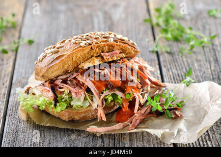 Cucina di strada: barbecue di carne di maiale tirato sandwich integrale con coleslaw, hot BBQ SAUCE servita su carta da imballaggio marrone su un sfondo di legno Foto Stock