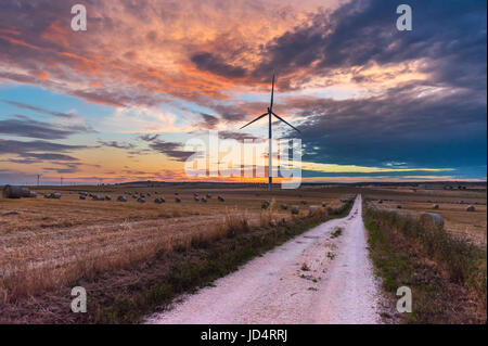 Puglia (Italia) - fattoria eolica con rock ruderi, le turbine eoliche e balle di fieno al tramonto Foto Stock