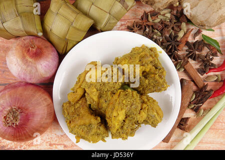 Piatto malese Rendang Ayam o a secco di pollo al curry e Ketupat Nasi (gnocco di riso) su sfondo di legno Foto Stock