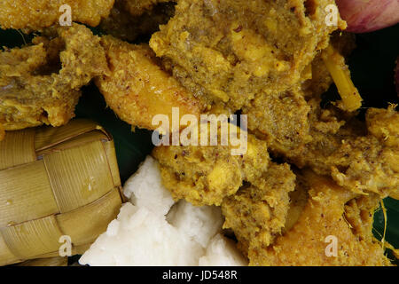 Piatto malese Rendang Ayam o a secco di pollo al curry e Ketupat Nasi (gnocco di riso) su sfondo di legno Foto Stock