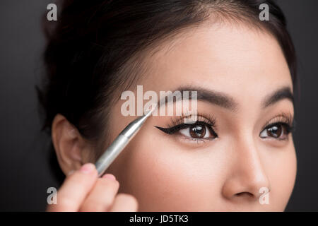 Chiusura del bel volto del giovane donna asiatica getting make-up. L'artista è l'applicazione di ombretto sul suo sopracciglio con spazzola Foto Stock