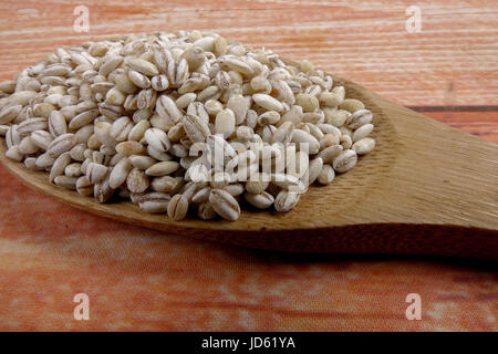 Organici di chicchi d'orzo su un cucchiaio di legno su sfondo di legno. Foto Stock