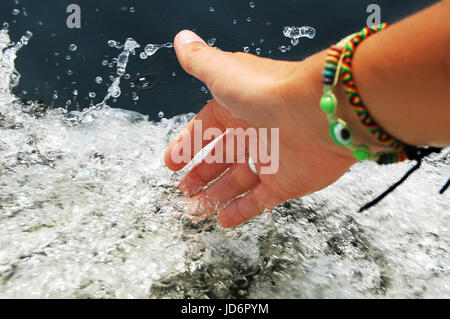 Mano femmina toccando gli schizzi di acqua di schiumatura mentre galleggiante sulla barca motore. Foto in primo piano. Foto Stock