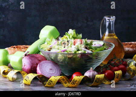 Ciotola di insalata di verdure, nastro di misurazione e verdi su un tavolo di legno - uno stile di vita sano concetto Foto Stock