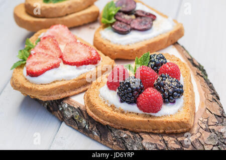 Cuore di biscotti a forma di diffusione con quark, fragole, more, lamponi e ciliegie e un rametto di menta e presentati su un disco ad albero Foto Stock