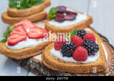 Cuore di biscotti a forma di diffusione con quark, fragole, more, lamponi e ciliegie e un rametto di menta e presentati su un disco ad albero Foto Stock