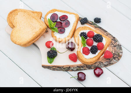 Cuore di biscotti a forma di diffusione con quark, ciliegie e un rametto di menta e presentati su un disco ad albero Foto Stock