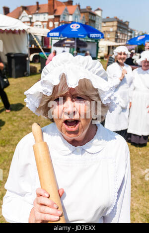 Le donne anziane vestite in cucina in stile vittoriano maid costume e azienda mattarello, arrabbiato e parlare, gridando, a viewer, il contatto visivo durante la Broadstairs Dickens Week Festival. Gli stati del militante cameriere. Foto Stock