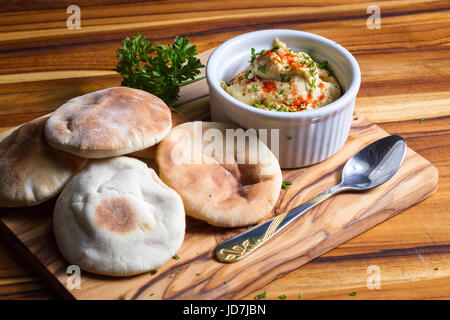 Ramekin riempito con hummus condito con paprica e prezzemolo come guarnire servita con piccolo pane pita tornate servita su una tavola di legno Foto Stock