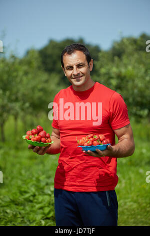 Felice agricoltore la presentazione di fragole appena raccolte dal suo giardino Foto Stock