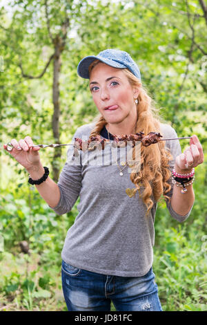 Bellissima ragazza con le lentiggini detiene un shish kebab e smorfie di lei con la lingua fuori Foto Stock